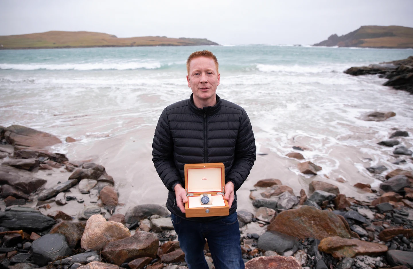 A prize recipient holding his open watch box on a rocky Channel Islands coast