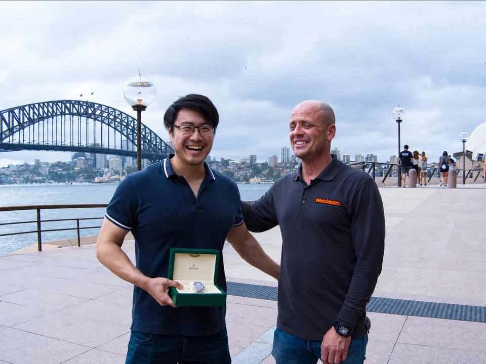 A Watchlotto winner holding his watch box with Jamie Robertson beside Sydney Harbour Bridge